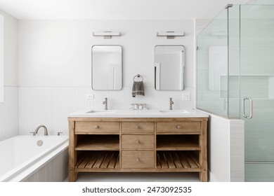 A bathroom with a natural wood cabinet with a white marble countertop, white herringbone tile around the tub, and a walk-in shower with large tiles.