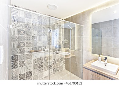 Bathroom Pattern Wall Design With Art Printed On The Wall In The Shower Area Which Covered With Glass Panels Under The White Ceiling And Walls. The Wooden Counter Drawer With Sink And Faucet