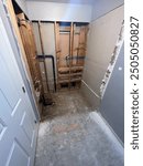 Bathroom renovation with exposed studs, plumbing, and unfinished flooring, showing ongoing demolition work