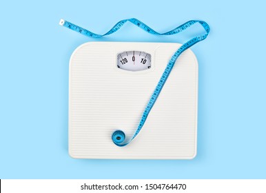 Bathroom Scales And Measuring Tape For Weight Loss Concept On Blue Background. Sport And Diet For Losing Weight. Bathroom Scale, Measuring Tape And Dumbbell. 