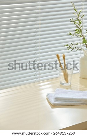 Bathroom setup with soft tile wall, towels, plant vase and toothbrushes. Light wood surface left empty for design mockups or wellness-themed product presentation.
