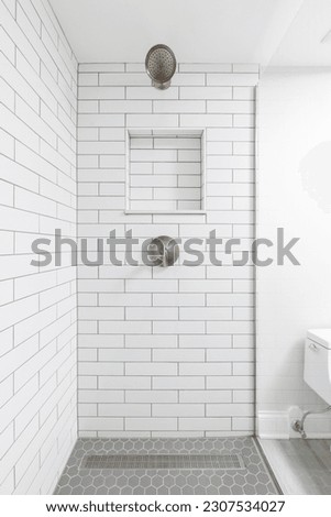 A bathroom shower with white subway tile walls, a built-in niche shelf, bronze shower head, and a grey hexagon tiled floor.