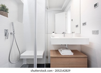 Bathroom with tiled shower in white tones with wooden cabinet and white washbasin in vacation rental apartment