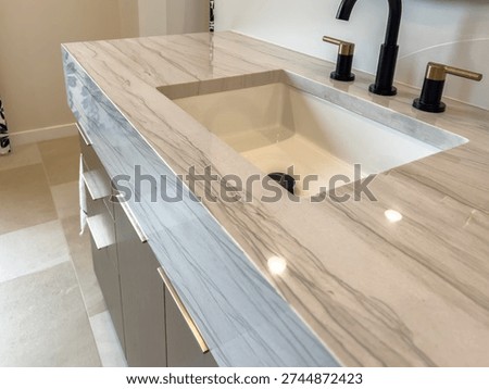 A bathroom vanity features a marble top with a built in sink and black fixtures. The design is modern, stylish, and minimal.
