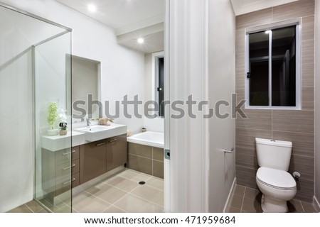Bathroom with washing area and the toilet of the luxurious house. Bathroom covers with the glasses from the left side and washroom included faucet over the mirror with a washstand near the bath tub.