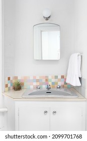 A Bathroom With A White Cabinet, Colorful Tiled Backsplash, And A Light Mounted Above The Mirror.