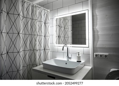 Bathroom In White Color. Large Washbasin. Mirror With Built-in Diode Tape Illumination Switching By Movement. Minimalist Style With Natural Wood Finish. Tiles And Painted Boards. Shower With Curtain.