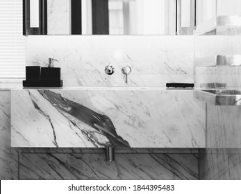 A bathroom with a white marble sink, thick bblack veins and black soap dispencer on top of the marble counter. high mirror and silver towel racks on the right hand side.