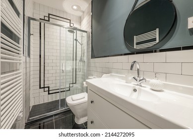 Bathroom With White Porcelain Sink And Contemporary Decoration With Round Mirror With Black Frame, Shower Cabin With Glass Screen And White Tiles