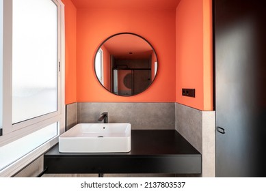 Bathroom With A White Porcelain Sink On A Black Wooden Countertop, A Walk-in Shower And A Round Mirror With A Black Frame To Match The Accessories Next To A White Aluminum Window