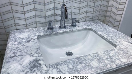 Weiße rechteckige Becken unter montiertem Einwaschbecken aus porzellanerischem Material mit Marmor- oder Granitsteindecke und poliertem Chromvorhang. Backsplash-Fliesen mit Pfeilmuster 