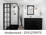 A bathroom with white walls, black cabinet and shower, marble subway tiles, and bronze sconces and faucet.