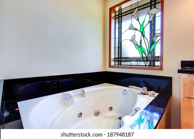 Bathroom With White Whirlpool Tub, Black Tile Trim Around It And Stained Glass Window