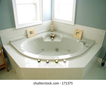 Bathroom with windows, white porcelain fixtures, plant, pastel walls, whirlpool bathtub with candles