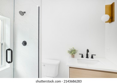 A Bathroom With A Wood Vanity, Gold Light Fixture, And A Marble Tiled Shower.