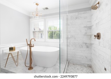 A bathroom's luxurious shower and bathtub. The standalone tub has a gold faucet and chandelier hanging above. The shower has subway and hexagon tiles. - Powered by Shutterstock