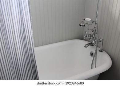 Bathtub Tap For Running Water In A White Clawfoot Tub With A Striped Curtain. 