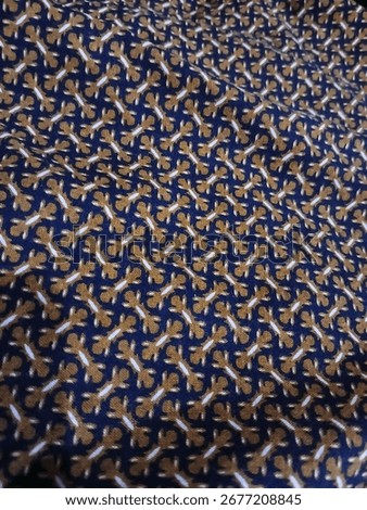 A Batik fabric with a dense, repeating pattern of small stylized figures in white and brown on a blue background.