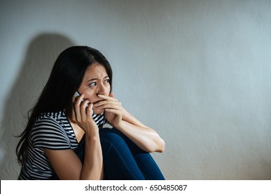 battered abused women concept - closeup photo of fear sadness woman having family violence problem using mobile cellphone calling police help in dark white background room.