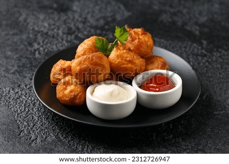 Battered chicken balls with tomato ketchup, mayonnaise on black plate. Party food