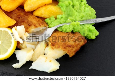 Battered cod fish fillet with chunky chips and mushy peas on a slate stone background