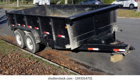 Battered Empty Black Industrial Dumpster Trailer Parked Curbside On Neighborhood Residential Street.