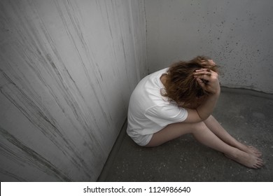 Battered young woman sitting alone on the concrete floor. Domestic violence. Woman in T-shirt and barefoot
