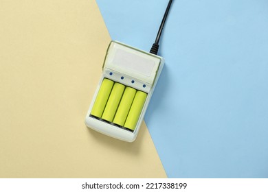 Battery charger with AA rechargeable batteries on blue yellow pastel background