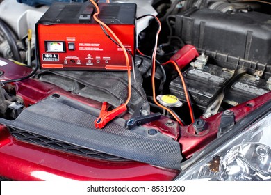 Battery Charger And Car In Auto Repair Shop.