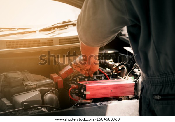 Battery charger and car in auto\
repair shop,Auto mechanic working in garage. Repair\
service.