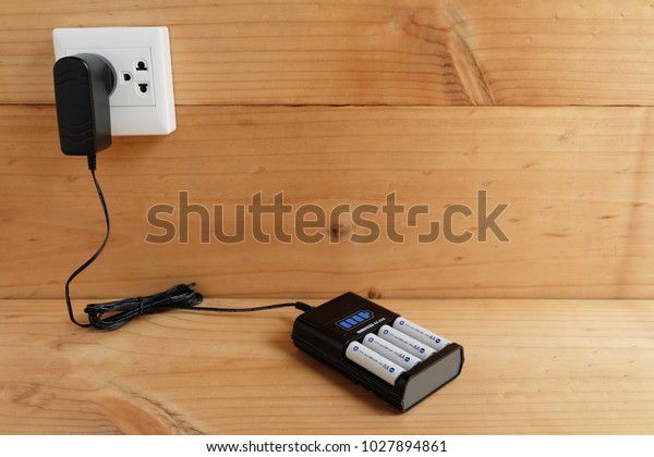 Battery Charger with\
battery size AA rechargeable with Charger Plug in power outlet\
adapter on wooden table