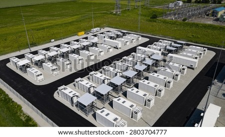 Battery energy storage system featuring rows of containerized units on a paved site, managing electricity flow and promoting grid stability, with an electrical substation in the background