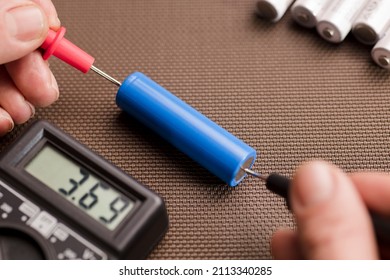 battery with volt calculator, voltmeter in the hands of a man, red positive pole, black negative pole, on a work table