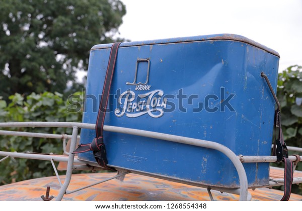 Battle Grounds, Washington \ USA - August 25 2018:\
Vintage blue Pepsi-Cola metal cooler latched onto a roof rack of a\
red rusty car