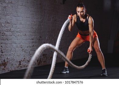 Battle ropes session. Attractive young fit and toned sportswoman training in gym