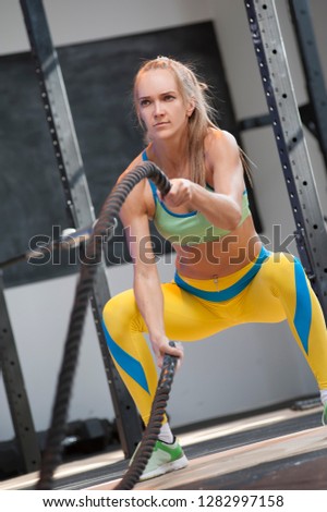 Similar – One young athletic woman at crossfit training, exercising with trx suspension fitness straps over dark background, front view, looking at camera