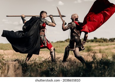 Battle With Spear And Sword Between Two Ancient Greek Or Roman Warriors In Battle Dress And Cloaks On Meadow.