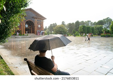 Batumi, Georgia - July 10, 2022: A Man Sits Under An Umbrella On A Bench In The Rain