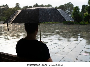 Batumi, Georgia - July 10, 2022: A Man Sits Under An Umbrella On A Bench In The Rain