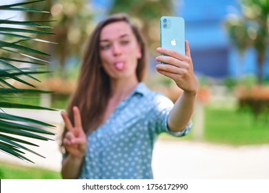 Batumi, Georgia - June 9, 2020. Modern Fun Woman Stick Out Tongue And Takes Selfie Photo On Iphone 11 Green Mint Color Outdoors