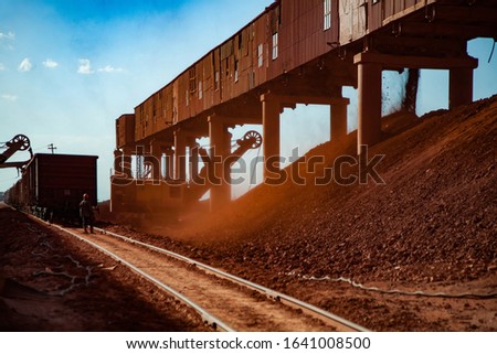 Bauxite clay open-cut mining. Loading and railway transporting terminal. Excavator loading aluminium ore. Hopper car train on rails. Worker controlling process.