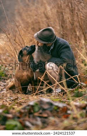 A bavarian man wearing a traditional folk costume interacting with his bavarian mountain dog nearby