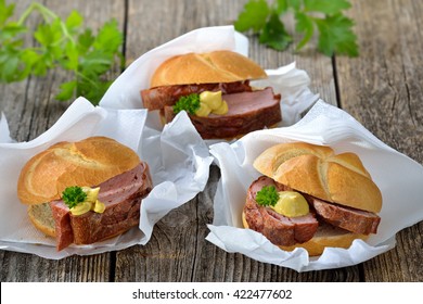 Bavarian takeaway food: Three rolls with baked meat loaf and mustard on wrapping paper with a napkin