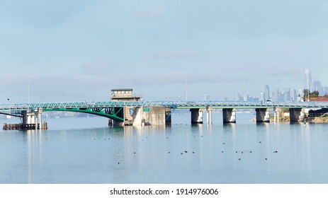 The Bay Farm Island Bridge In Alameda. A 125 Foot Single Leaf Bascule Bridge, It Spans The San Leandro Bay Inlet To The Oakland Estuary At Otis Drive In Alameda, CA. San Francisco Cityscape Behind.