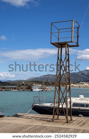 Bay with a harbor. Turquoise water of the Ionic sea. Iron tower and a boat. Mountains in the background. Blue sky with white clouds. Astrakeri, Corfu, Greece.