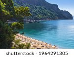 Bay near Jaz beach near Budva on the background of rocky hills covered with trees, calm blue sea. Blue cloudless morning sky, rows of straw umbrellas. Montenegro, Mediterranean sea