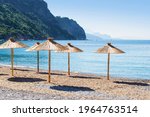 Bay near Jaz beach near Budva on the background of rocky hills covered with trees, calm blue sea. Blue cloudless morning sky, rows of straw umbrellas. Montenegro, Mediterranean sea