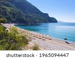 Bay near Jaz beach near Budva on the background of rocky hills covered with trees, calm blue sea. Blue cloudless morning sky, rows of straw umbrellas. Montenegro, Mediterranean sea