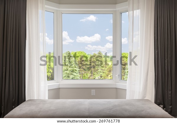 Bay window with drapes, curtains and view of trees\
under summer sky