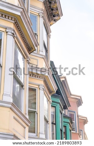 Bay windows of victorian townhouses against the white sky background at San Francisco, CA. Row of colorful old townhouses with dentils and single hung windows.